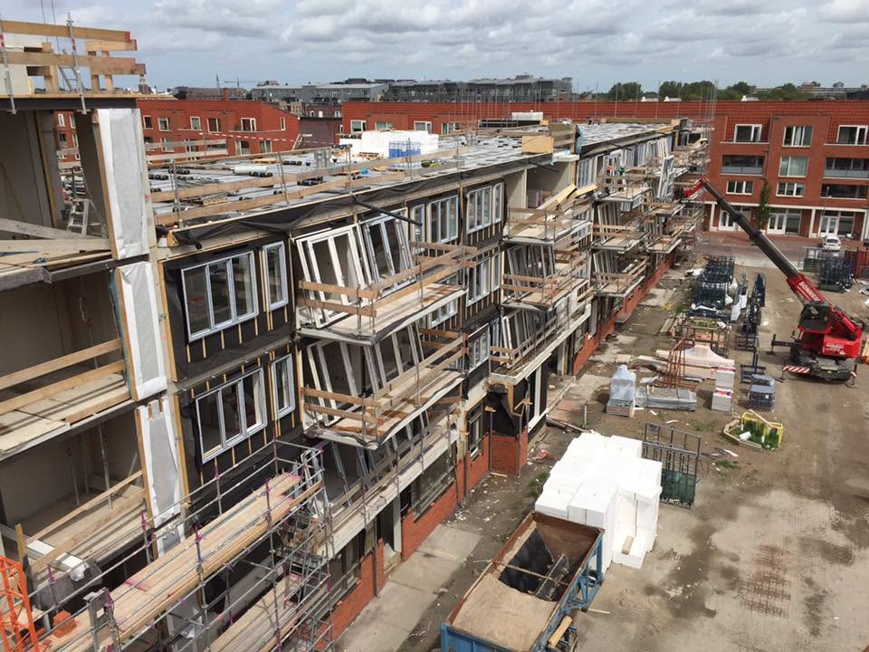 Rij nieuwbouwwoningen in aanbouw met steigers en houten dakconstructies